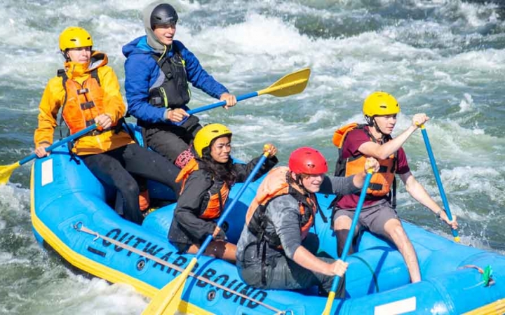 a group of gap year students use paddles to navigate whitewater on an outward bound course